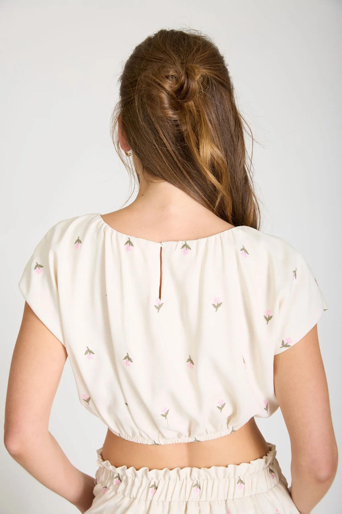 Woman wearing a cream-colored blouse with a subtle pattern on a plain background
