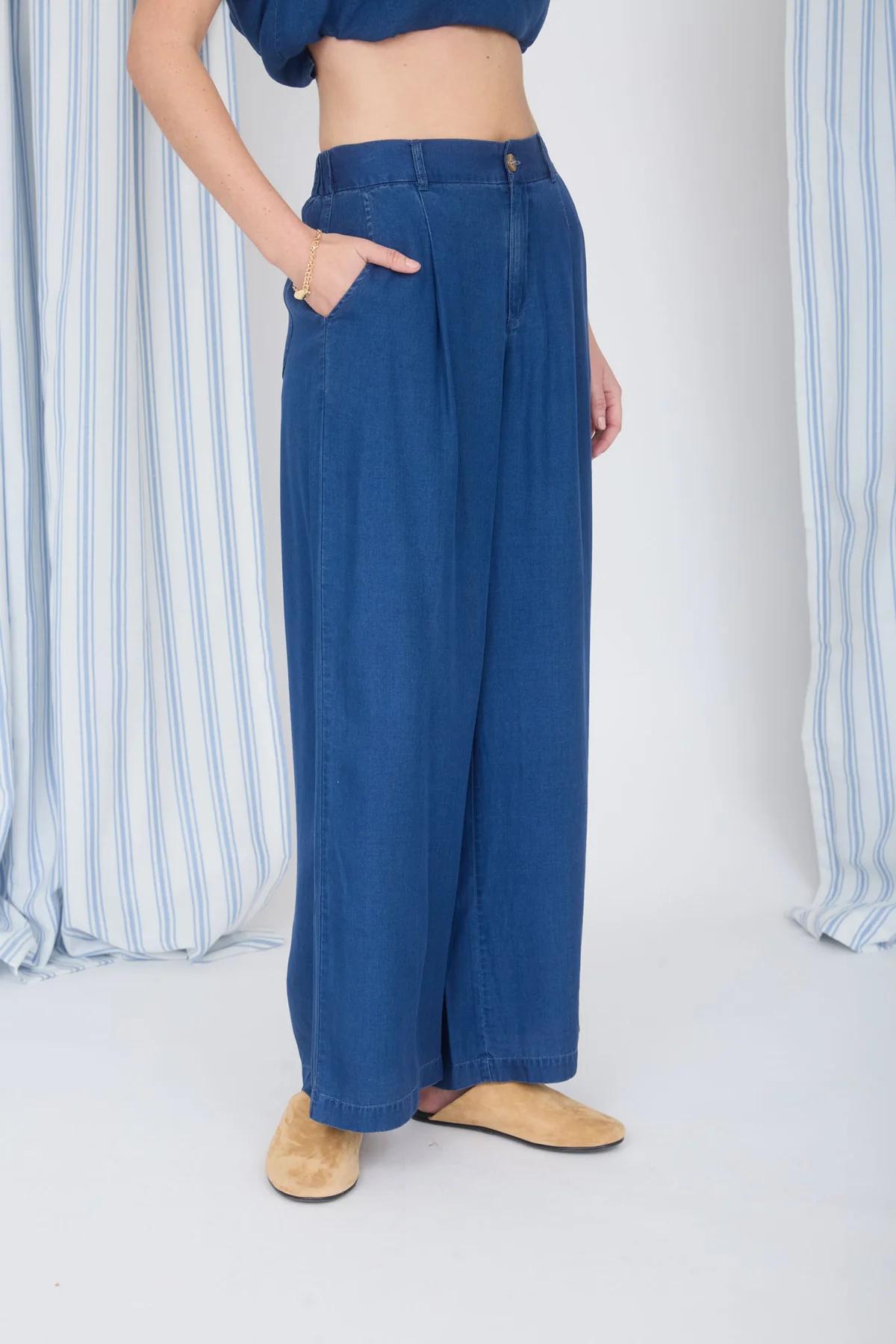 Person wearing blue wide-leg jeans with a striped curtain background