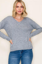 Woman wearing a gray sweater and blue jeans against a plain background